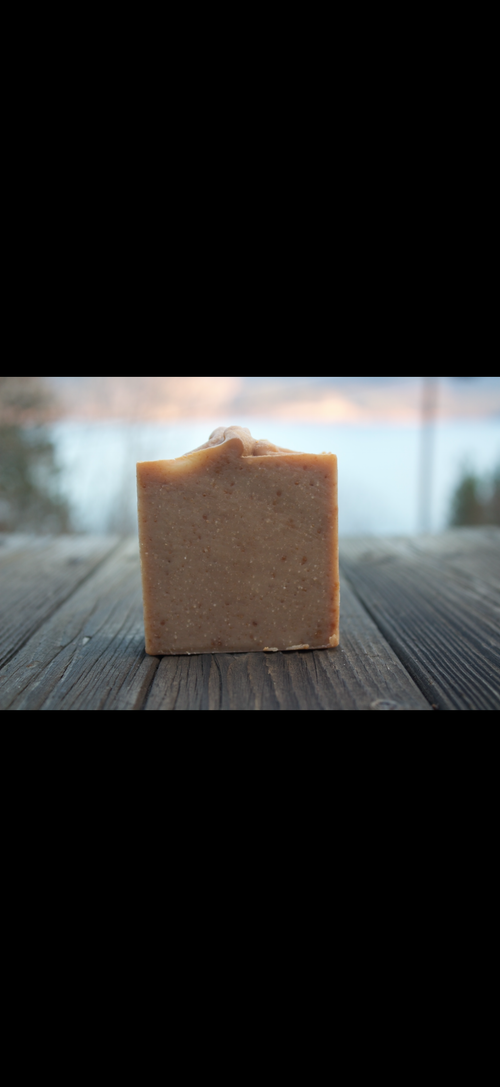 Square bar of soap on a wooden surface with a blurred natural background