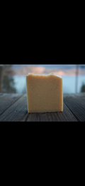 Square block of soap on a wooden surface with a blurred natural background